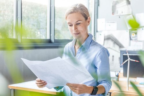 Eine Frau schaut lächelnd auf einen großes Blatt Papier, dass sie vor sich in den Händen hält. Im Hintergrund ist ein Windrad zu sehen.