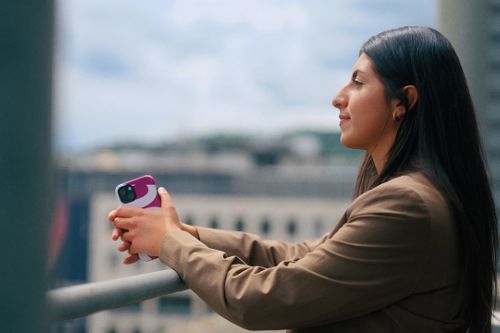 Eine junge Frau mit Smartphone in der Hand schaut in die Ferne.