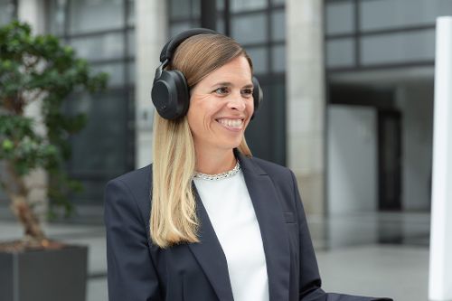 Eine Frau im Blazer nimmt mit Headset an einem Video-Telefonat teil.