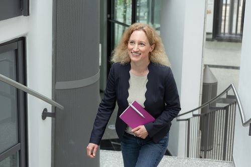 Eine Frau mit einem Notizbuch in der Hand geht eine Treppe nach oben.