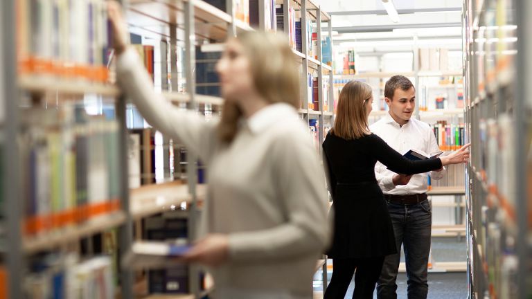 Studierende zwischen Bücherregalen der Bibliothek