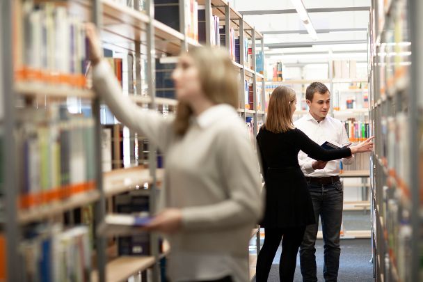 Studierende zwischen Bücherregalen der Bibliothek