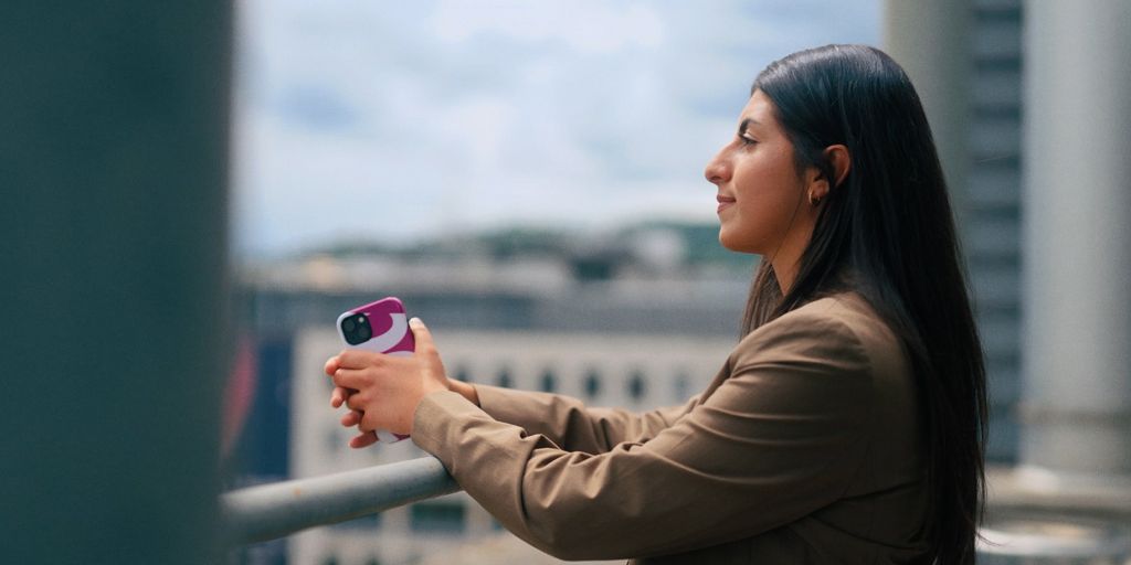 Eine junge Frau mit Smartphone in der Hand schaut in die Ferne.