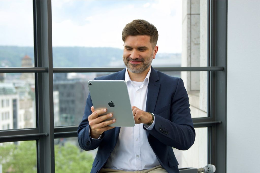 Ein Mann sitzt vor einem Fenster und tippt auf einem iPad.