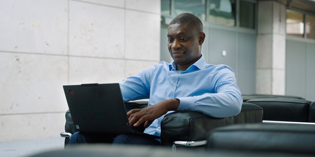 Ein Mann mit Hemd sitzt mit einem Laptop in einem modernen Lounge-Bereich und arbeitet.