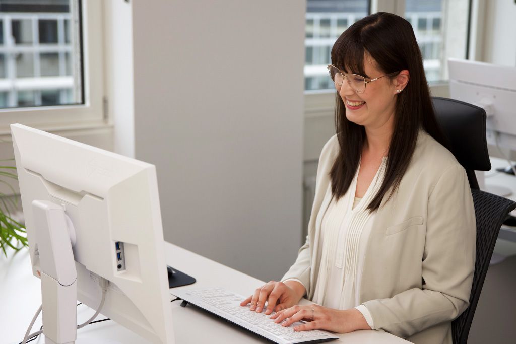 Eine junge Frau arbeitet an einem Desktop-Computer an einem modernen Arbeitsplatz in einem hellen Büro.