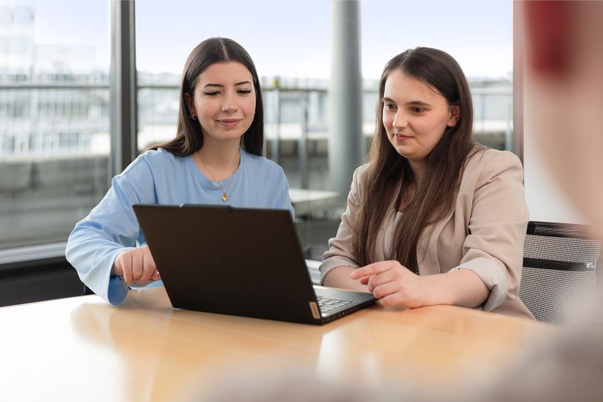 Eine junge Frau zeigt einer anderen jungen Frau etwas auf einem Laptop.