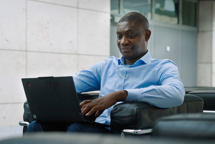 Ein Mann mit Hemd sitzt mit einem Laptop in einem modernen Lounge-Bereich und arbeitet.