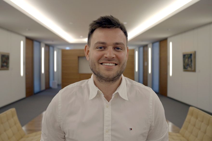 Ein Portrait von einem lächelnden Mann, im Hintergrund ist ein Besprechungszimmer zu sehen