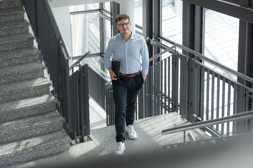 Mann in Hemd in einem Treppenhaus in einem Bürogebäude mit Laptop unter seinem Arm.