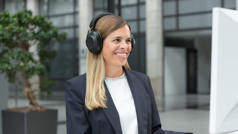 Eine Frau im Blazer nimmt mit Headset an einem Video-Telefonat teil.