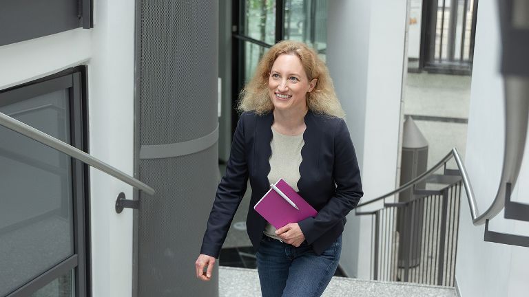 Eine Frau mit einem Notizbuch in der Hand geht eine Treppe nach oben.