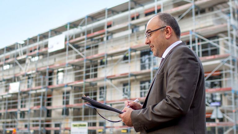 Immobiliengutachter Abdullah Ayhan mit Klemmbrett neben Immobilie