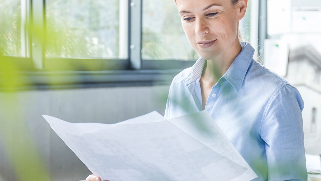 Frau liest Dokumente im Büro zwischen Pflanzen.