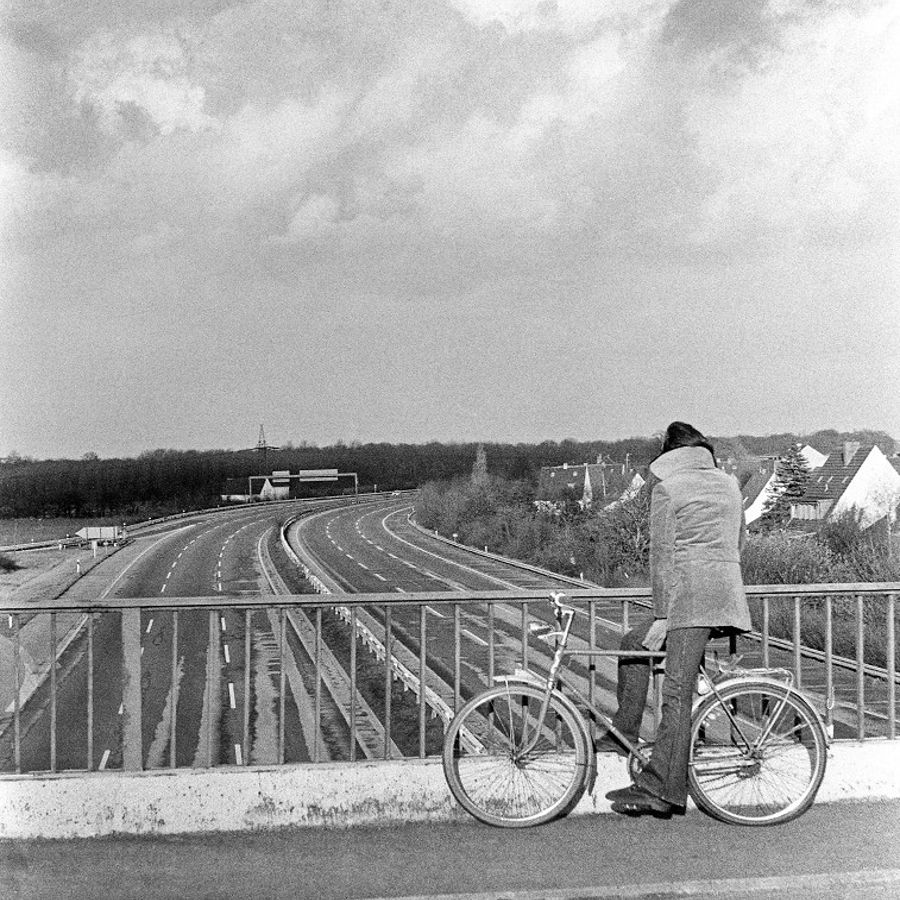 Eine Person schaut auf einem Fahrrad von einer Brücke auf eine leere Autobahn