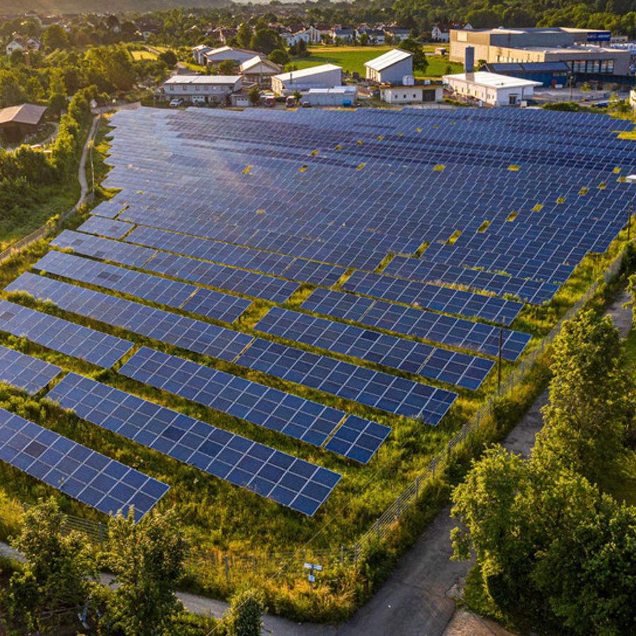 Eine große Solaranlage umgeben von Wiesen, Bäumen und vereinzelten Gebäuden